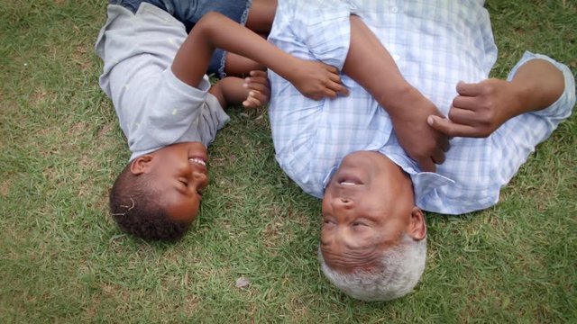 Black grandad and grandson play lying on grass, aerial view