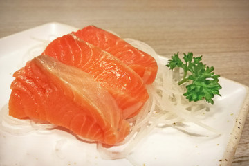 Salmon sashimi sliced on white julienned radish on white paper plate.