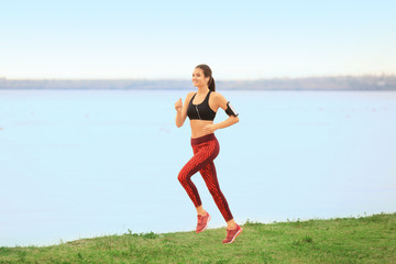 Young sporty woman running on river shore