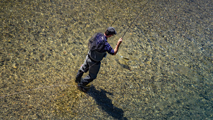 Angler mit Wathose im Wasser beim Angeln mit Fliegenrute bei Sonne im klaren Fluss stehend und werfend