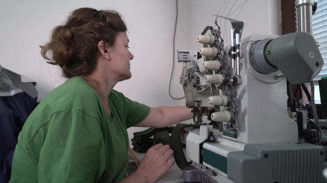 Close up of middle aged Caucasian woman during sits at sewing machine and tailoring, dressmaker stitching cloth in workshop, portrait, interior scene
