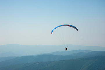 A paraglider flies over a mountain valley on a sunny summer day. Paragliding in the Carpathians in the summer.