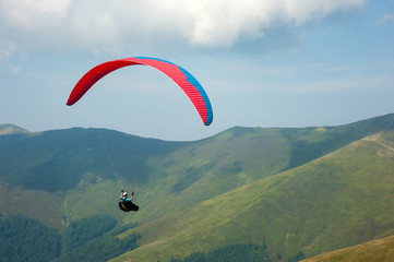 A paraglider flies over a mountain valley on a sunny summer day. Paragliding in the Carpathians in the summer.