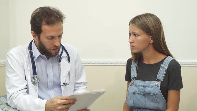 The doctor informs the patient about the tests results. The patientseems really worried. The doctor is trying to calm her down.The young woman comes to the therapist. They are sitting in doctors