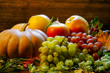 bright pumpkins, grapes and apples on branches and grass on a wooden background. halloween