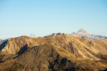 High altitude pasture, rocky mountain peaks and jagged ridge, with scenic sky, the Italian Alps. Expansive view in backlight. Toned desaturated image.