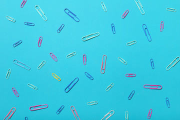Multi coloured paper clips on blue background, flat lay