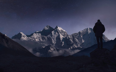 A man contemplating the mountains under the moonlight in a starry night
