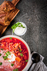 Traditional Ukrainian Russian vegetable soup borscht, with hard cream. parsley rye bread rolls, on black stone table, copy space top view