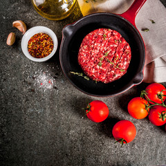 Raw organic beef meat burgers cutlets  with spices, thyme, tomatoes, olive oil in frying pan on black background, top view copy space