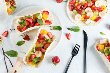 Summer snacks. Food for a party. Fruit tacos with strawberries, mangoes, bananas, chocolate, mint. On a light blue concrete table. Copy space top view