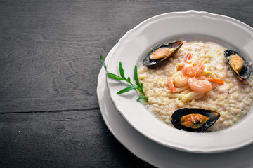 Fototapeta na wymiar Risotto with seafood, shrimp, mussels and squids and cheese. On a wooden background. Top view. Free space.