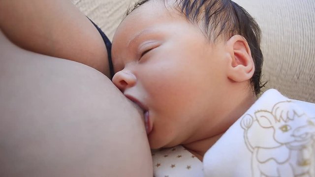 Little baby sucks milk from nipple of mother breast.
