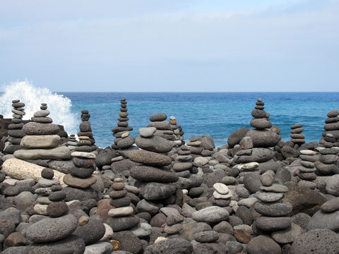 rock art piles and towers of grey stones and pebbles on a beach with blue sky and blue sky in tenerife with breaking waves