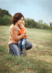 Fototapeta premium Mom and his little son are hugging on the background of a green glade.
