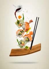 Crédence de cuisine en verre imprimé Bar à sushi Flying sushi pieces served on wooden plate, separated on soft background