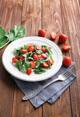 Plate with strawberry spinach salad on wooden table