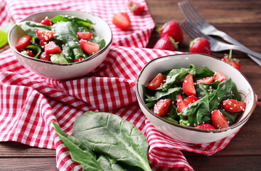 Bowls with strawberry spinach salad on wooden table