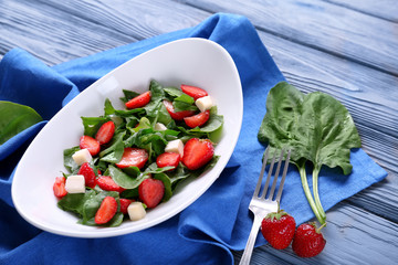 Plate with strawberry spinach salad on wooden table