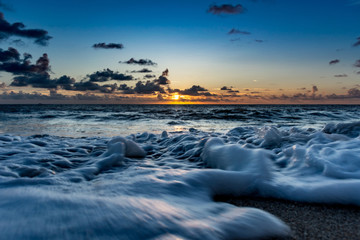 close up of moving bubbles and sea foam on a wave crashing on the sand just after sunrise
