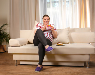 Obraz premium Overweight young woman eating sweets on sofa at home