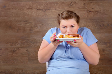 Overweight young woman eating sweets on wooden background