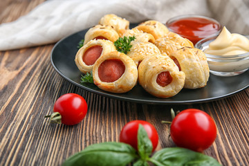 Plate with delicious sausage rolls on table