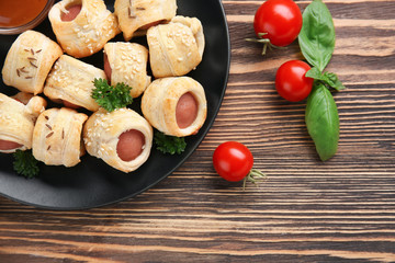 Plate with delicious sausage rolls on wooden background