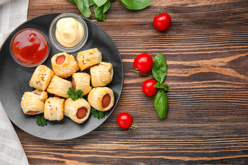 Plate with delicious sausage rolls on wooden background