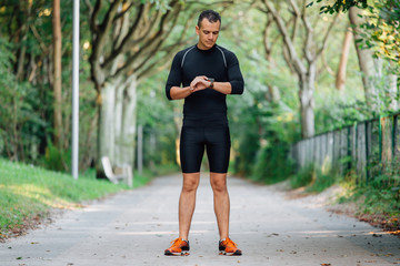 Athlete runner looking at heart rate monitor watch. Sportsman using smartwatch during morning exercise.