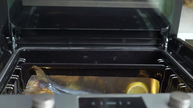 Cooking whole roasted fish seriola with lemon baked in the oven. View from above of chef hands places baking sheet with raw fish into the oven removes cooked amberjack from the oven. Edited sequence.