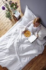 model in white bed eating pizza