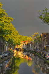 Fototapeta na wymiar Travel Concepts and Ideas. Traditional Dutch Channels Located in Old City Delft. Picture Taken During amazing Picturesque Sunlight Straight After the Rain with Grey Clouds.