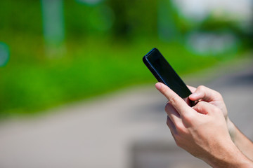 Closeup of male hands is holding cellphone outdoors on the street. Man using mobile smartphone.