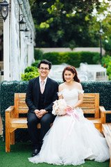 The bride and groom sitting on the chair in the garden background. Asian wedding couple on the chair in the garden background.