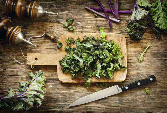 Chopped kale leaves on wooden cooking board, top view