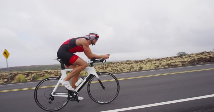 Triathlon cycling - male triathlete biking on triathlon bike. Fit man cyclist on professional triathlon bicycle wearing time trail helmet for ironman race. From Big Island Hawaii. SLOW MOTION RED EPIC