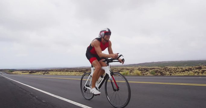 Cycling Triathlon man - male triathlete biking on triathlon bike. Fit man cyclist on professional triathlon bicycle wearing tri suit and time trail helmet training for ironman. From Big Island, Hawaii