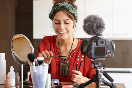 Gorgeous female does make up, sits in front of camera, has online translation on website, shared beauty tips with followers, uses free internet connection. Modern technology, video blogging concept