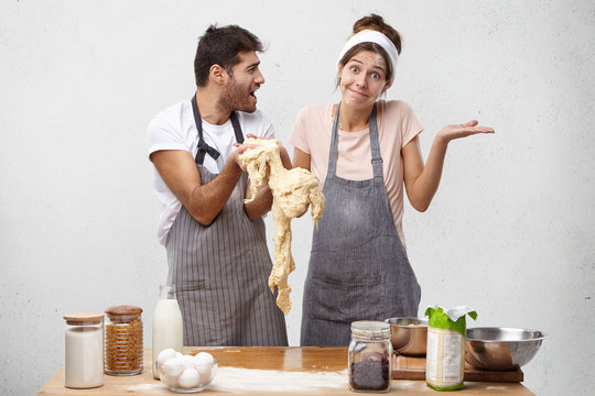 Puzzled woman shrug shoulders as holds dough, doesn`t know what she did wrong and angry chef shoutes at her, promises to punish for bad work. Female cooker ingnores recipe, has complete failure