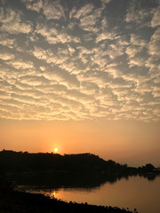 High cumulus cloud, orange sky, lake and sun at sunset