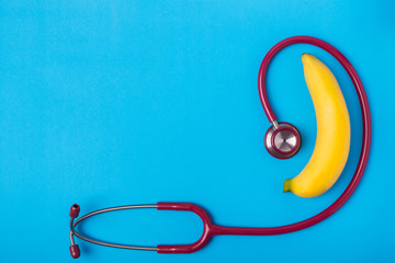 Stethoscope and yellow banana on blue background. For men penis check up concept. With empty free space for text or design. Top view
