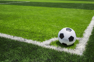 Fototapeta na wymiar Soccer ball on artificial bright and dark green grass at public outdoor football or futsal stadium