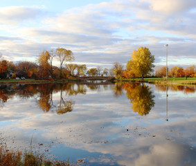 Autumn nature background. Beautiful fall landscape in the city park. Colored trees and cloudy sky reflected in  the water during sunset. Midwest USA, Wisconsin.