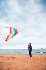 cute little boy plays with a kite on the ocean coast in cold weather