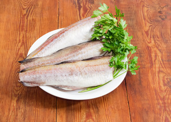 Uncooked carcasses of the Alaska pollock and parsley on dish