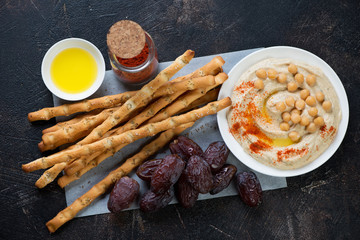 Above view of salted breadsticks with homemade hummus and date fruits, horizontal shot
