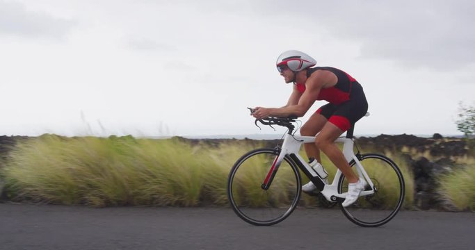 Cyclist biking in Triathlon - male triathlete cycling on triathlon bike. Fit man cyclist on professional triathlon bicycle wearing time trail helmet for ironman race. Big Island Hawaii. SLOW MOTION.