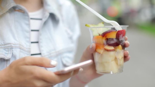 Close-Up. Woman Used a Phone and Holds a Glass of Fresh Fruit