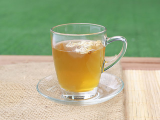Chrysanthemum juice in glass cup on wood background against green grass background in the garden.